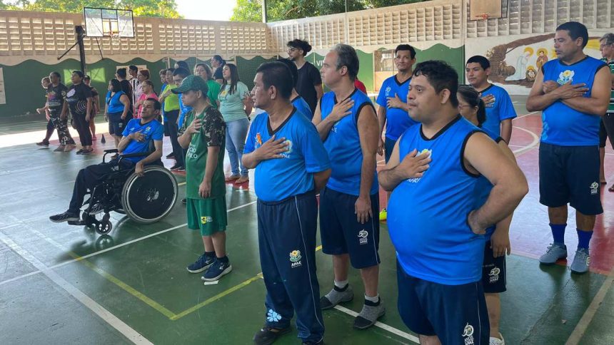 Grupo de pessoas, algumas em cadeiras de rodas, com a mão no peito, em um evento da APAE Manaus.