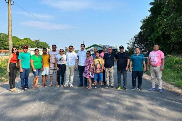 Grupo de pessoas posando para foto em estrada pavimentada, com céu azul ao fundo.