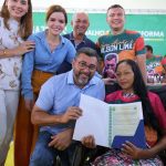 Grupo de pessoas sorrindo e segurando documentos em evento público.