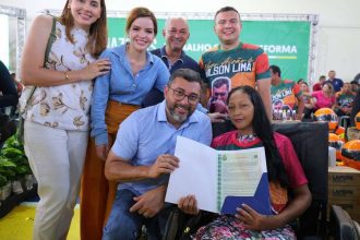 Grupo de pessoas sorrindo e segurando documentos em evento público.