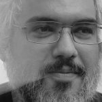 Homem de meia-idade com óculos e barba, em foto preto e branco.