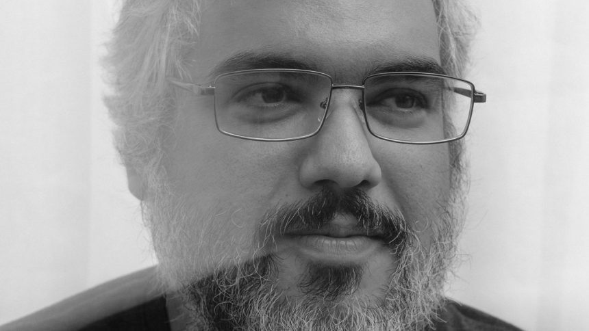 Homem de meia-idade com óculos e barba, em foto preto e branco.