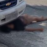 Homem deitado no chão perto de carro, fingindo estar morto para escapar após roubo.