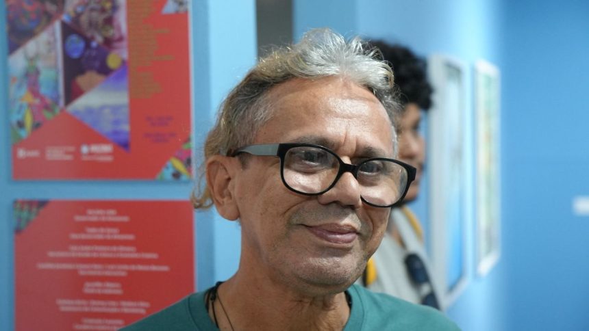 Homem sorrindo com óculos em evento de arte na Casa das Artes.