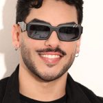 Homem sorrindo com óculos escuros em evento musical.