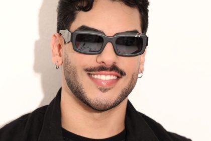 Homem sorrindo com óculos escuros em evento musical.