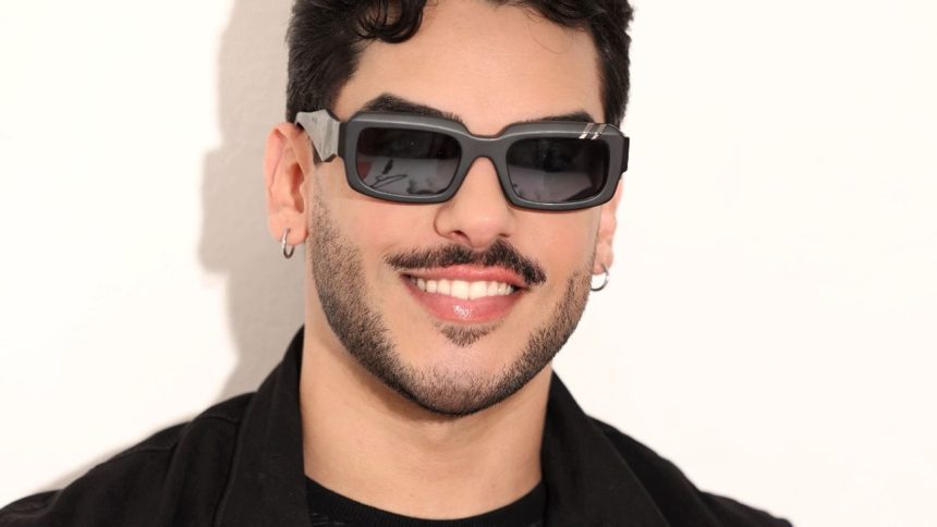 Homem sorrindo com óculos escuros em evento musical.