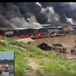 Incêndio em estruturas à beira-rio no Amazonas, com fumaça densa e fogo visível.
