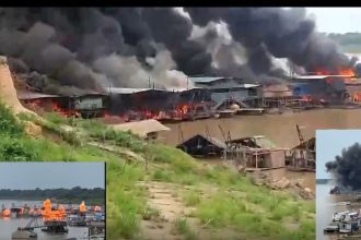 Incêndio em estruturas à beira-rio no Amazonas, com fumaça densa e fogo visível.