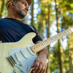 Instrumentista manauara com guitarra em floresta, concentrado