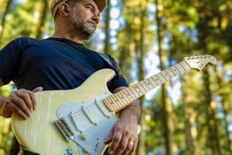 Instrumentista manauara com guitarra em floresta, concentrado