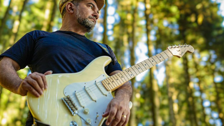 Instrumentista manauara com guitarra em floresta, concentrado
