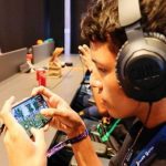 Jogador de Free Fire em evento de games com fone de ouvido e celular.