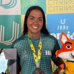 Kathleen Amaral com medalha de bronze no JUBs Praia 2025, segurando um troféu e um mascote.