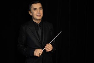 Maestro em um terno preto segurando uma batuta.