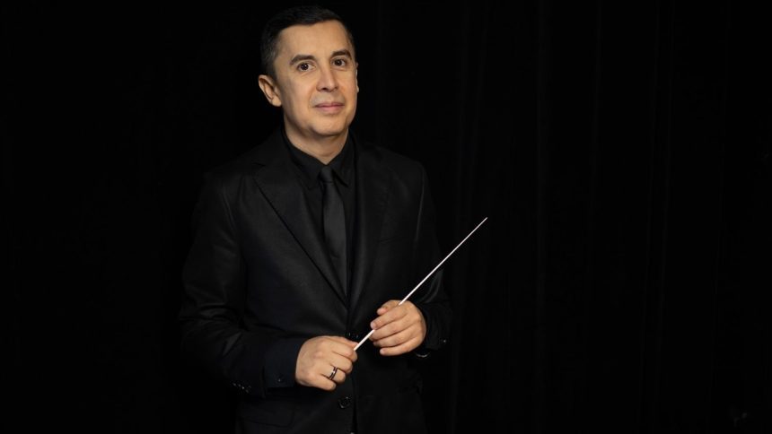 Maestro em um terno preto segurando uma batuta.