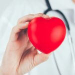 Médico segurando um coração vermelho, simbolizando a saúde cardiovascular no Setembro Vermelho.