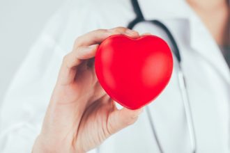 Médico segurando um coração vermelho, simbolizando a saúde cardiovascular no Setembro Vermelho.