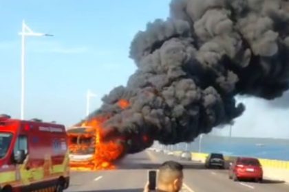 Ônibus em chamas na ponte Jornalista Phelippe Daou, com fumaça preta intensa e ambulância no local.