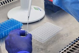 Pesquisador usando pipeta em laboratório, com placas e tubos.