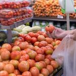 Pessoa escolhendo tomates em supermercado, com foco na variedade de produtos.