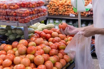 Pessoa escolhendo tomates em supermercado, com foco na variedade de produtos.