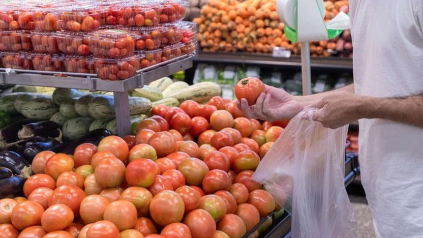 Pessoa escolhendo tomates em supermercado, com foco na variedade de produtos.