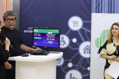 Pessoas em evento com tela mostrando dados de sorteio, incluindo nomes e valores.