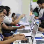 Pessoas em processo seletivo simplificado, utilizando laptops e preenchendo formulários.