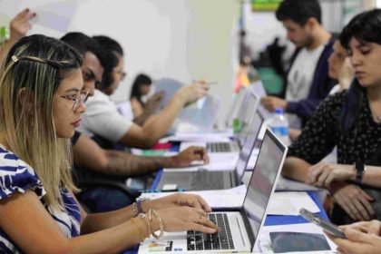 Pessoas em processo seletivo simplificado, utilizando laptops e preenchendo formulários.