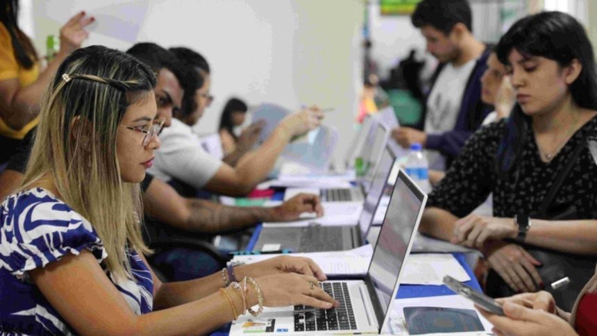 Pessoas em processo seletivo simplificado, utilizando laptops e preenchendo formulários.