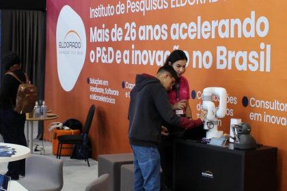 Pessoas observando robôs em um estande do Instituto Eldorado, com logotipo em destaque. Foco em inovação e tecnologia.