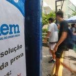 Placa do Enem (Exame Nacional do Ensino Médio) com estudantes ao fundo.