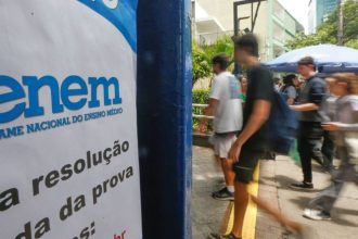 Placa do Enem (Exame Nacional do Ensino Médio) com estudantes ao fundo.