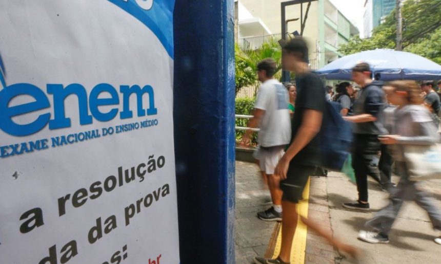 Placa do Enem (Exame Nacional do Ensino Médio) com estudantes ao fundo.