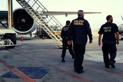Policiais federais em ação em um aeroporto, com avião ao fundo.