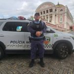 Policial militar em frente a viatura com o Teatro Amazonas ao fundo.