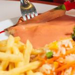 Prato com carne, molho, acompanhamentos e talheres.