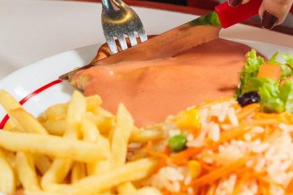 Prato com carne, molho, acompanhamentos e talheres.