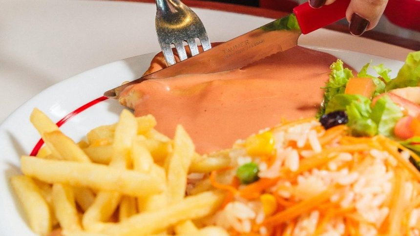 Prato com carne, molho, acompanhamentos e talheres.