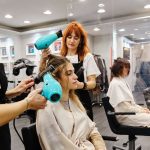 Profissionais de beleza trabalhando em um salão, usando secadores de cabelo.