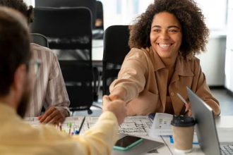 Profissional sorrindo cumprimenta colega em ambiente de trabalho durante anúncio de vagas de emprego.