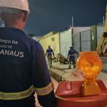 Trabalhadores da Águas de Manaus em obras na Avenida Noel Nutels à noite, com sinalização de segurança.