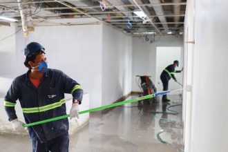 Trabalhadores pintando paredes em um canteiro de obras, usando equipamento de proteção.