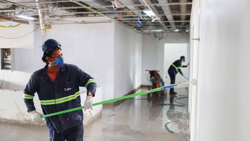 Trabalhadores pintando paredes em um canteiro de obras, usando equipamento de proteção.