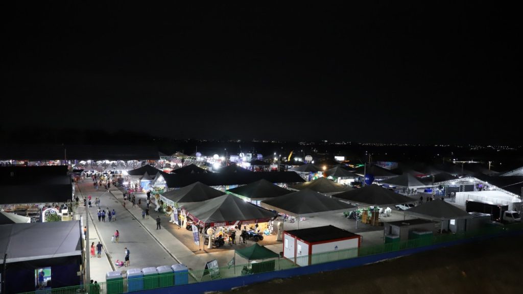 Vista noturna da Expoagro, evento de agronegócio com barracas e multidão.