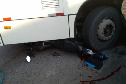 Acidente de trânsito em Manaus: moto esmagada sob ônibus, com sangue no chão.