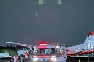 Ambulância e avião Cessna Grand Caravan estacionados em um aeroporto à noite.