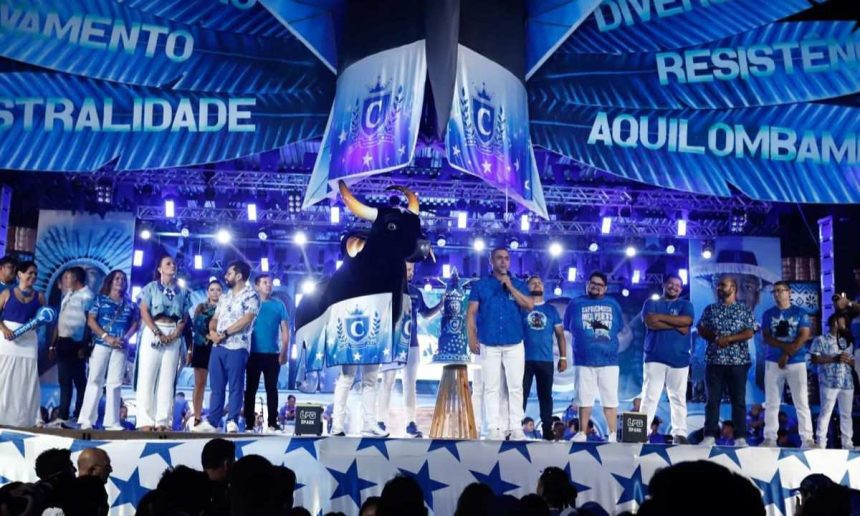 Anúncio do tema do Caprichoso para o Festival de Parintins 2026 com palco azul e figuras.