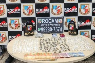 Apreensão de drogas: diversos pacotes e dinheiro sobre uma mesa, com emblemas da Rocam ao fundo.